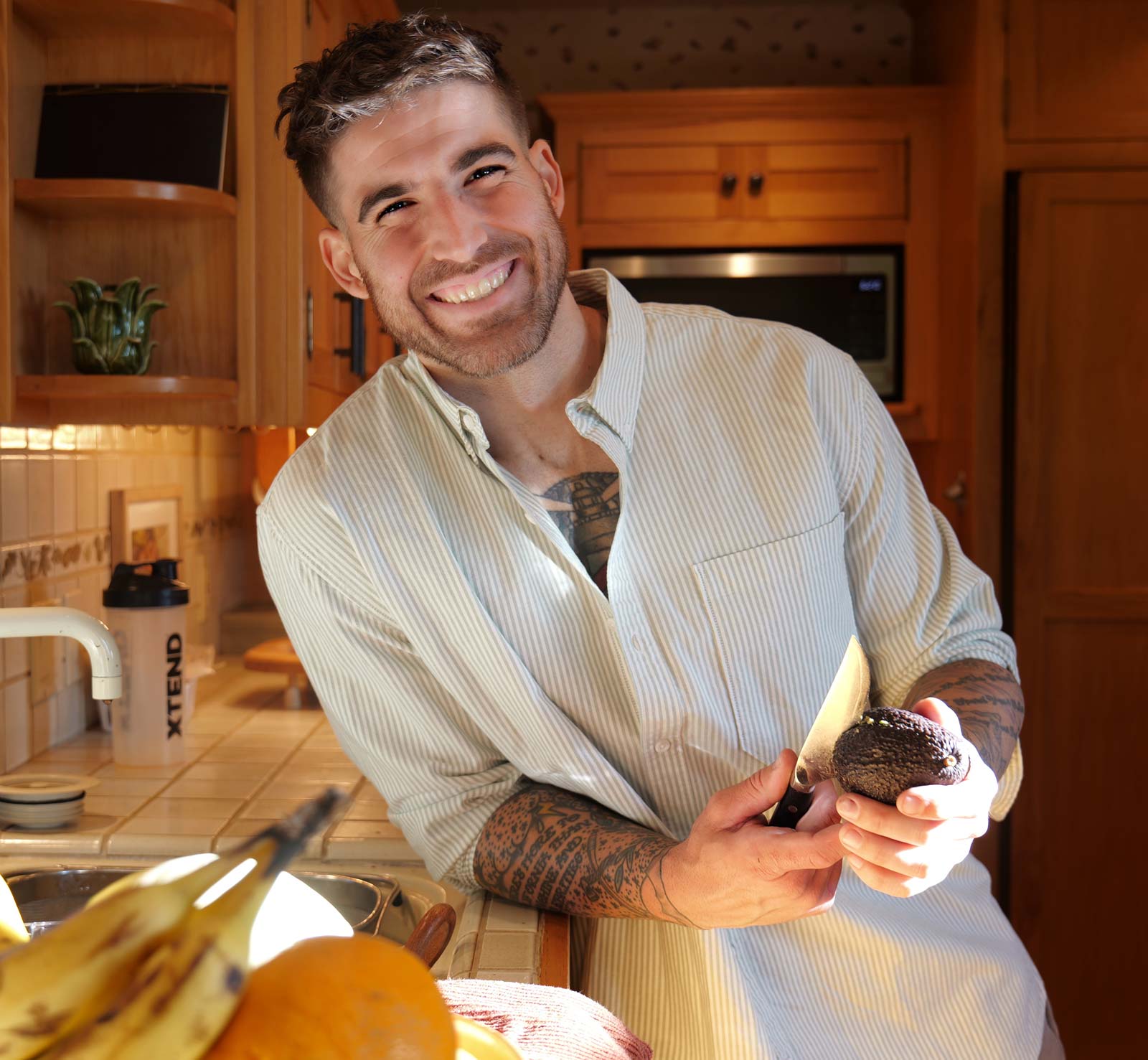 A picture of the smiling coach in kitchen holding avocado