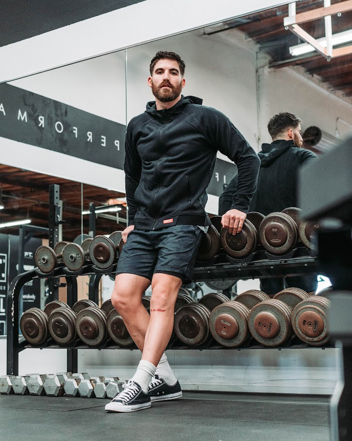 A picture of the coach posing in front of the weights